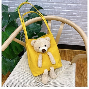 Detailed view of yellow canvas tote bag featuring a 3D plush teddy bear on a woven chair