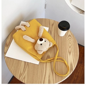 Detail of yellow canvas tote bag with a cute 3D plush bear on a wooden cafe table