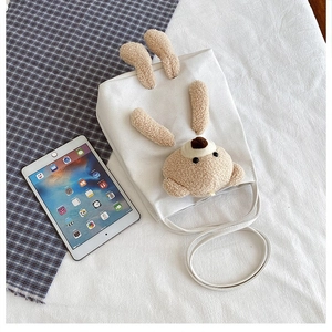 Close-up of white canvas bag with fuzzy 3D bear showing capacity next to tablet