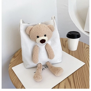 Detail shot of a white canvas tote bag featuring a 3D plush teddy bear on a wooden table