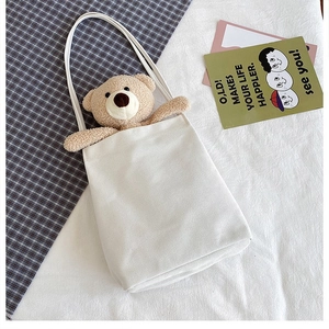 Detail of white canvas tote bag featuring a cute plush teddy bear tucked into the top pocket
