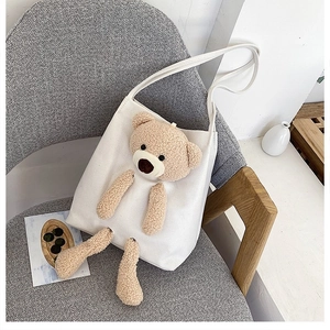Detailed close-up of a white canvas tote bag with a 3D plush brown bear attachment