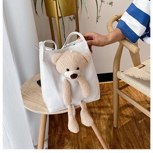 Detail of white canvas tote with 3D plush bear design on a rustic wooden table