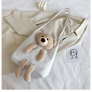 Flat lay of white canvas bear handbag with plush teddy bear on a minimalist background