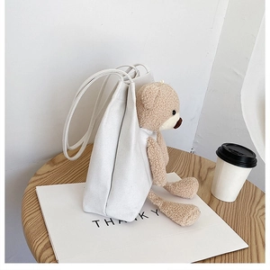 Detailed view of a white canvas shoulder bag with a cute brown plush teddy bear charm