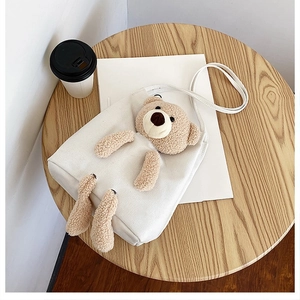Detail of white canvas tote featuring a 3D plush teddy bear on a wooden cafe table