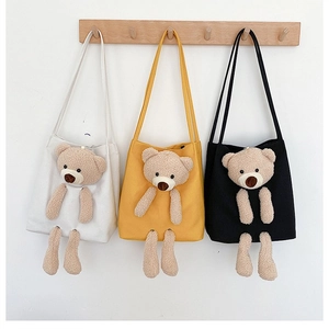 Detailed view of three canvas tote bags in white, yellow, and black with plush bear decor