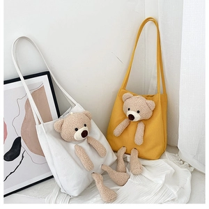 Detail of white and yellow canvas tote bags featuring 3D plush bear and long straps