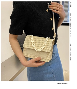 Détail du sac bandoulière en paille tressée beige avec chaîne décorative et boucles dorées