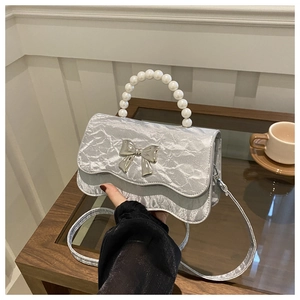 Detail of silver pleated handbag with faux pearl handle and metal bow clasp