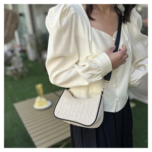 Detail of cream woven half-moon crossbody bag with black trim and wide nylon strap