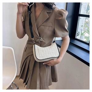 Detail of a beige woven tote bag with black trim and adjustable strap worn by a model