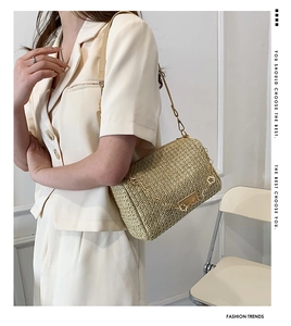 Detail of beige woven crossbody bag with gold chain and floral metal pendant accent
