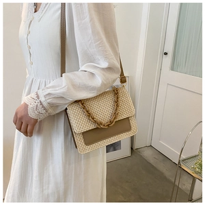 Détail du sac bandoulière en paille avec chaîne résine sur une robe en dentelle