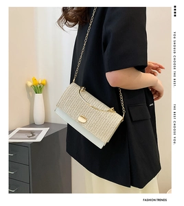 Gros plan d'un sac bandoulière en paille tissée et cuir blanc avec chaîne dorée porté