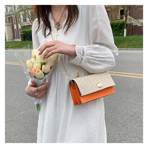 Détail de la texture tissée beige et du rabat orange avec chaîne dorée sur le sac