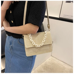 Détail du sac en paille beige avec chaîne blanche épaisse et boucle en métal doré