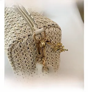 Detail of golden metal hardware and white leather strap on a beige woven crossbody bag