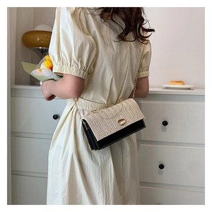 Détail du sac bandoulière en paille tressée avec chaîne dorée sur une robe crème