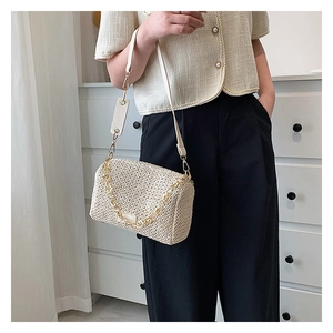 Détail du sac bandoulière beige tressé avec chaîne dorée porté par un mannequin
