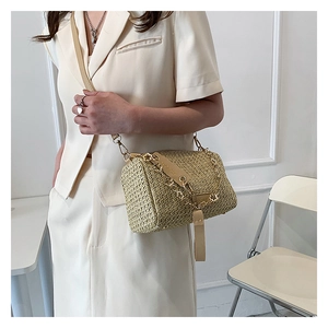 Détail du sac bandoulière en paille tressée avec chaîne dorée et étiquette en cuir chic