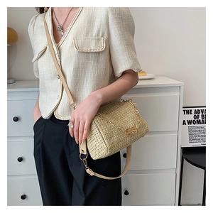 Détail d'un sac bandoulière tissé beige avec chaîne dorée porté par un mannequin