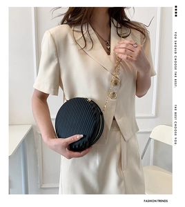 Détail d'un sac rond plissé avec chaîne dorée sur mannequin en costume beige