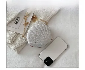 Mini shell-shaped crossbody bag with silver sequins and gold chain next to a smartphone
