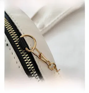 Gros plan sur la garniture métallique dorée et le zip de ce petit sac rond blanc