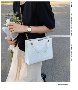 Close-up of white crocodile pattern tote bag with gold chain strap on an elegant model