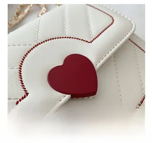 Détail du sac matelassé blanc avec fermoir cœur rouge et bandoulière chaîne dorée