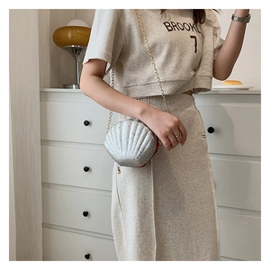 Detail of silver shell-shaped bag with gold chain strap and pearl charm on a model