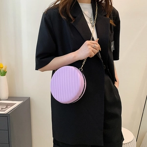 Détail d'un sac rond violet avec bandoulière chaîne dorée porté sur un blazer noir