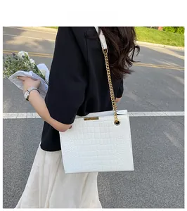 White crocodile pattern tote bag with gold chain strap shown in an outdoor street setting