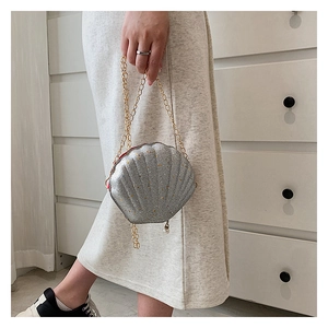 Detail view of silver shell-shaped bag with gold chain and elegant pearl zipper pull