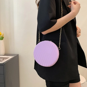 Détail d'un sac bandoulière rond plissé violet avec chaîne dorée porté par un mannequin