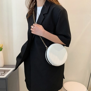 Gros plan d'un sac rond blanc à rayures texturées et chaîne dorée porté par un mannequin