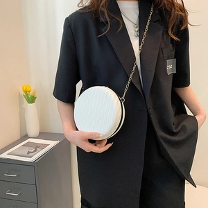 Gros plan d'un sac rond blanc en cuir avec chaîne dorée porté sur un blazer noir chic