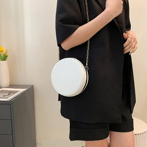 Détail du sac rond plissé blanc avec bandoulière dorée porté par un mannequin en intérieur