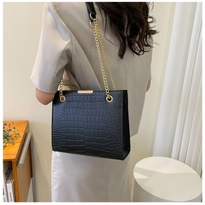 Detail shot of black crocodile pattern leather tote bag with gold chain strap in indoor setting