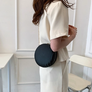 Détail d'un sac rond noir plissé en satin avec une fine bandoulière chaîne dorée