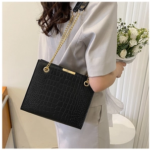 Detail of black crocodile pattern tote bag featuring gold chain straps and metal trim
