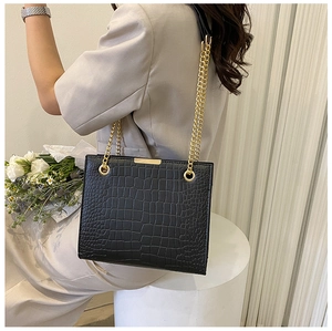 Detail of black crocodile pattern tote bag with gold chain strap on cream background