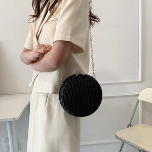 Détail du sac à main rond noir avec texture plissée et chaîne dorée porté par un mannequin