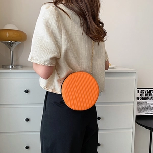 Gros plan du petit sac rond orange vif avec texture plissée et bandoulière en chaîne dorée