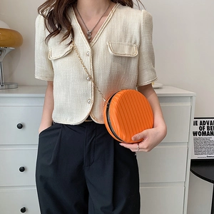 Vue détaillée du sac rond orange avec texture à rayures verticales et bandoulière chaîne