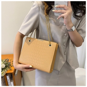 Detail of light beige crocodile pattern leather handbag with elegant gold chain strap