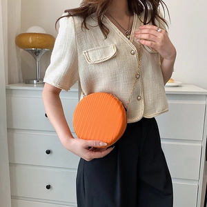 Détail d'un petit sac rond orange vif avec texture verticale et bandoulière en chaîne dorée