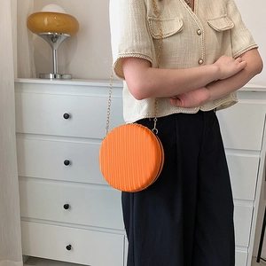 Détail du sac à bandoulière rond orange avec texture nervurée et chaîne en métal doré
