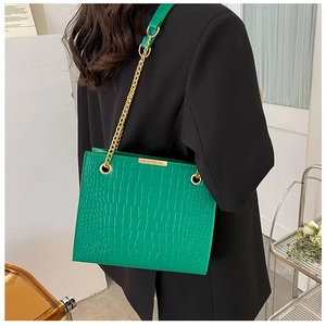 Detail of green crocodile texture shoulder bag with gold chain strap on a model
